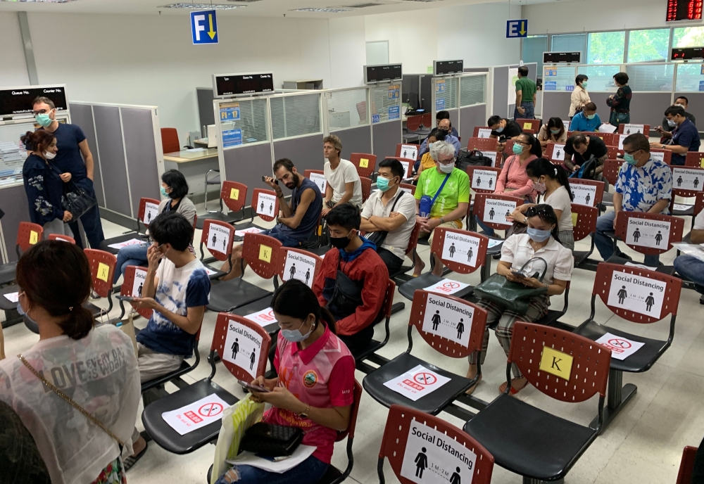 People wear face masks while waiting as chairs are marked for applicants to observe social distance at the Immigration Office in Bangkok on March 24, 2020, as Thailand moves to close its borders after a spike in the number of COVID-19 coronavirus cases in