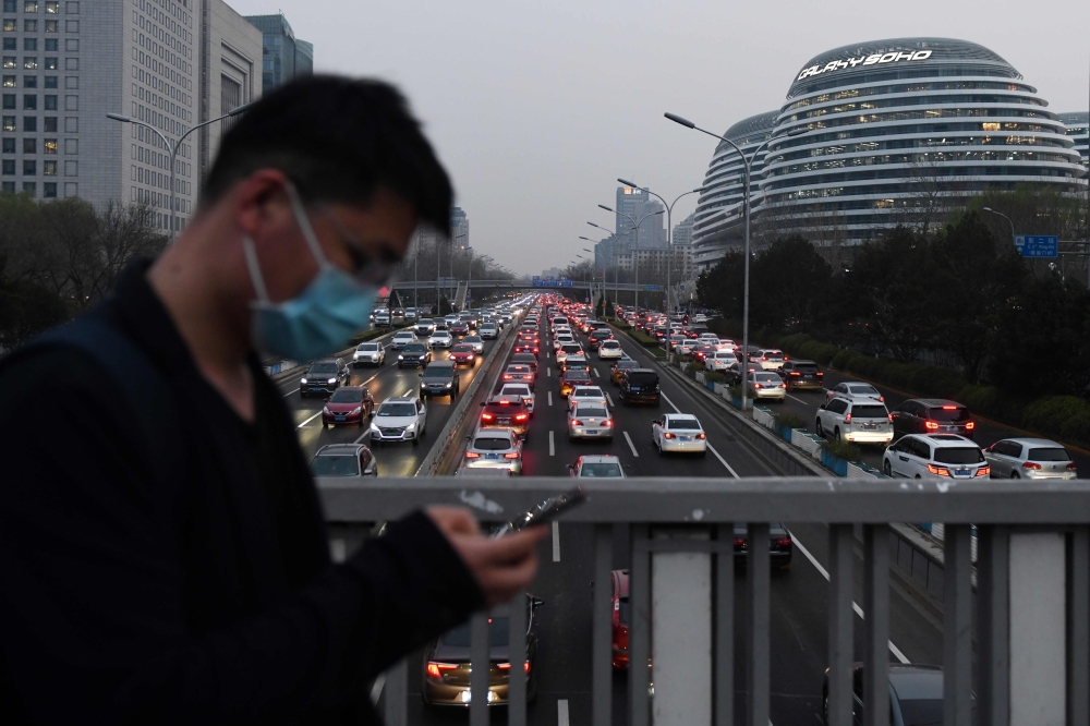 A man walks past wearing a face mask as cars crowd the Second Ring Road in Beijing amid the ongoing COVID-19 coronavirus outbreak on March 24, 2020.   AFP / GREG BAKER

