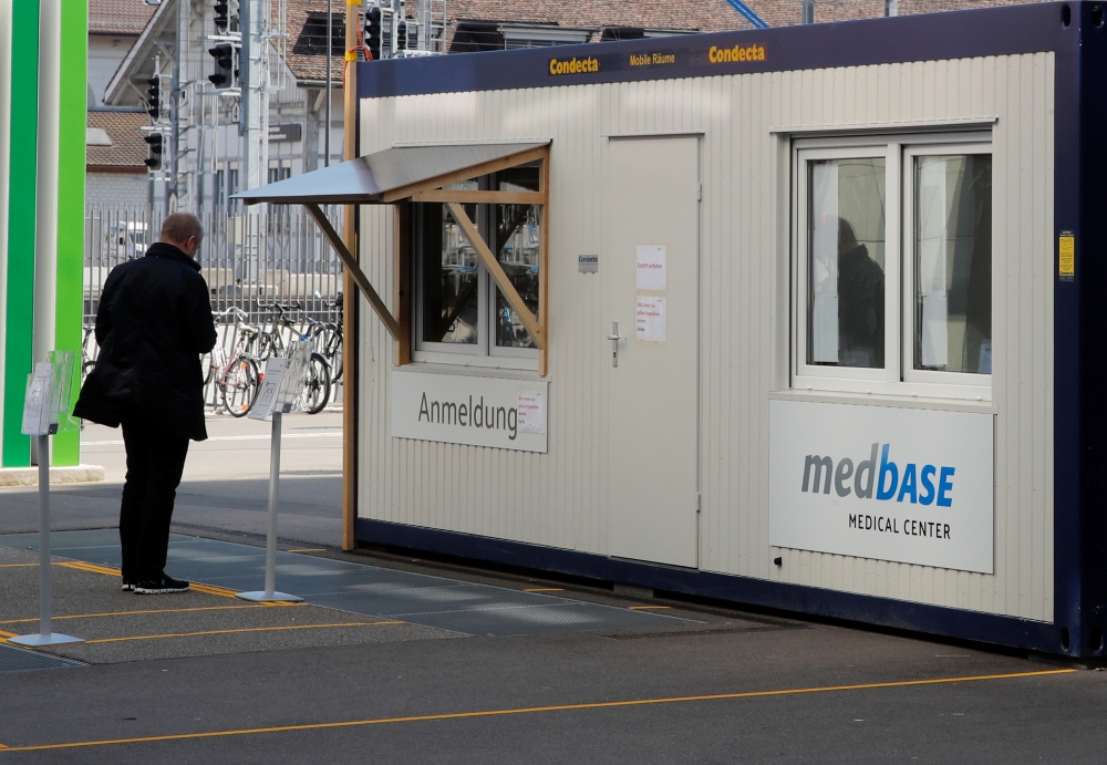 A man waits in front of a container of Medbase medical center, used for tests on coronavirus disease (COVID-19) on a square in Winterthur, Switzerland March 24, 2020. REUTERS/Arnd Wiegmann