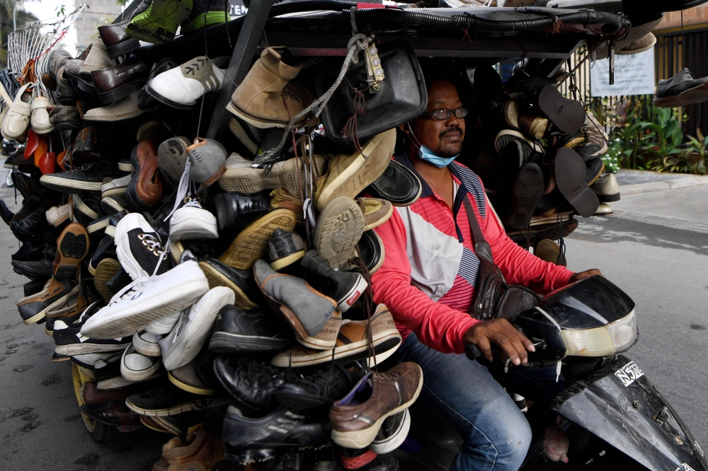 A man rides a motorcart loaded with secondhand shoes for sale along a street in Phnom Penh on March 24, 2020. AFP / Tang Chhin Sothy 