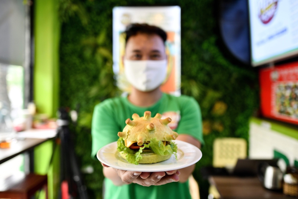 Pizza Home restaurant owner Hoang Tung poses with a coronavirus-themed burger in Hanoi on March 26, 2020, amid restrictions being put in place to contain the spread of the COVID-19 coronavirus. / AFP / Manan Vatsyayana 
