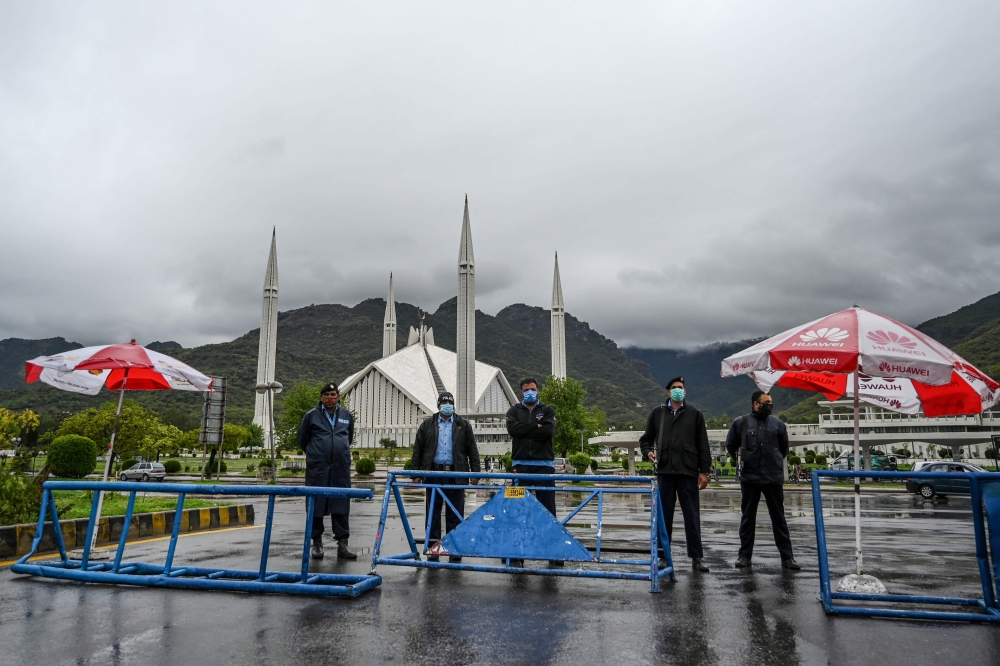 Policemen wearing facemasks stand guard at a checkpoint beside the Grand Faisal Mosque during a government-imposed nationwide lockdown as a preventive measure against the COVID-19 coronavirus, in Islamabad on March 27, 2020. / AFP / Aamir QURESHI
