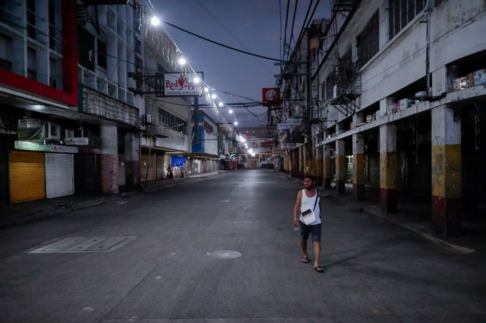 FILE PHOTO: A man wearing a protective mask on his neck walks past closed shops in an empty street following the lockdown in the Philippine capital to prevent the spread of the coronavirus disease (COVID-19), in Manila, Philippines, March 24, 2020. REUTER