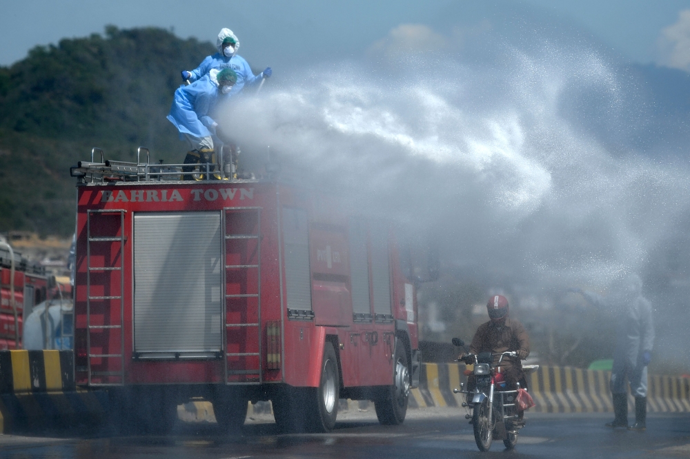 Workers wearing protective gear spray disinfectant on a street at a residential area during a government-imposed nationwide lockdown as a preventive measure against the COVID-19 coronavirus, in Islamabad on March 29, 2020. / AFP / Aamir QURESHI