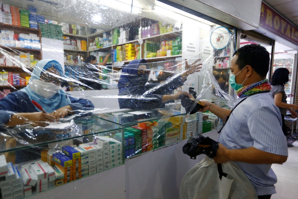 A customer wearing protective face mask makes his transaction through a plastic barrier as a preventive measure against the coronavirus disease (COVID-19) in Jakarta, Indonesia, April 2, 2020. REUTERS/Ajeng Dinar Ulfiana