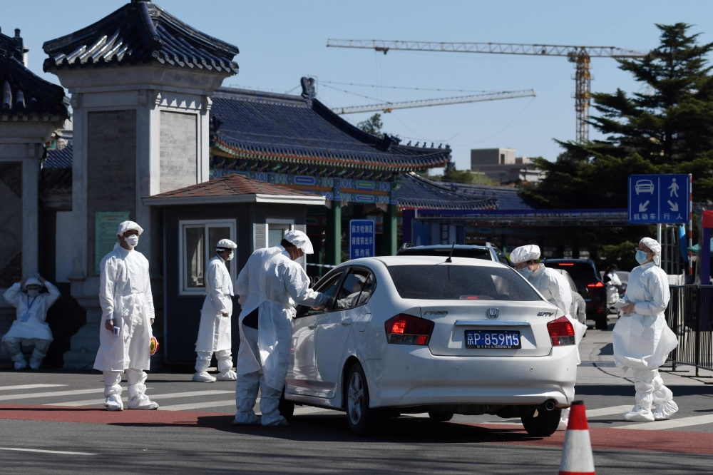 Workers wearing protective suits as a preventive measure against the COVID-19 coronavirus take the temperature of people arriving at the Babaoshan Revolutionary Cemetery in Beijing on April 3, 2020. / AFP / GREG BAKER