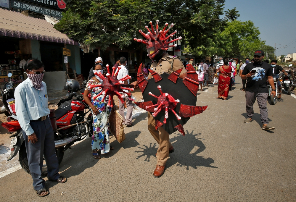 A police officer wearing a helmet and holding shields depicting coronavirus walks in a market area to advice people to maintain safe distance during a 21-day nationwide lockdown to slow the spreading of coronavirus disease (COVID-19) in Chennai, India, Ap