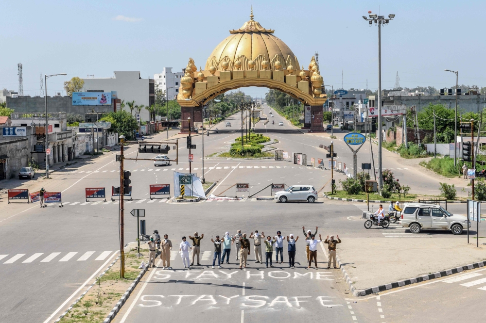 Police personnel along with members of National Human Rights and Crime Control Organization pose for photographs while gesturing behind a slogan 'Stay Home Stay Safe' written on the road at the Golden Gate (background) during a government-imposed nationwi