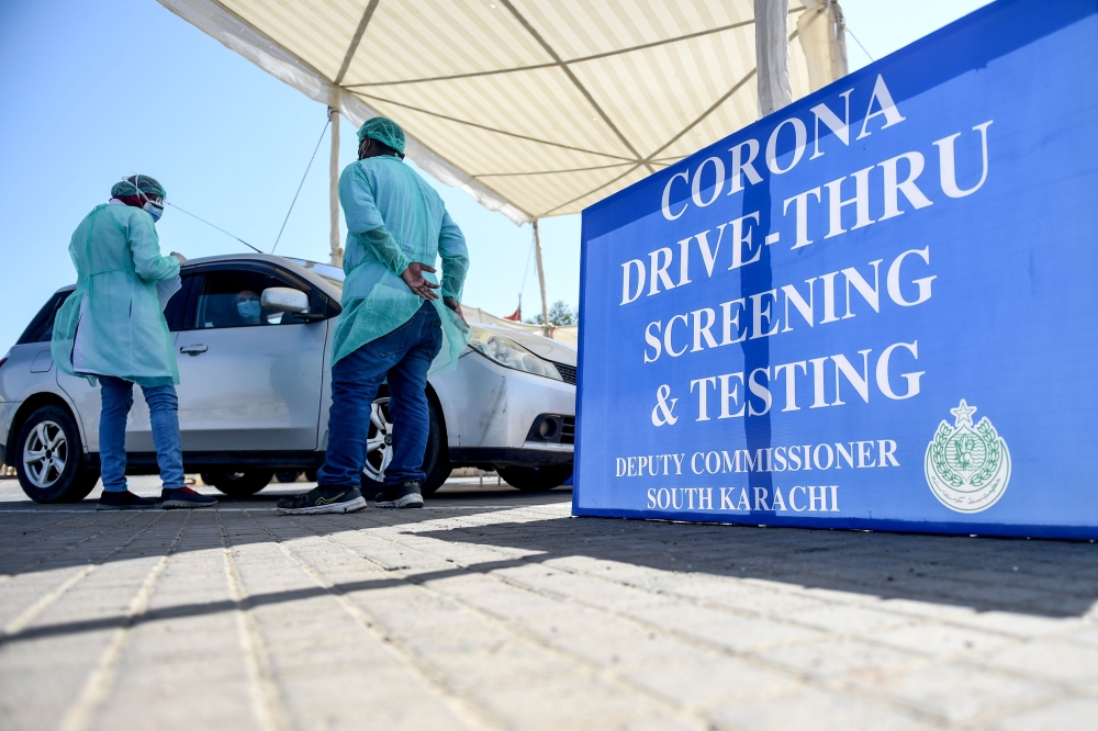 Medical staff members wearing protective gear take information from a resident sitting in a car for a coronavirus test at a drive-through screening and testing facility point during a government-imposed nationwide lockdown as a preventive measure against 