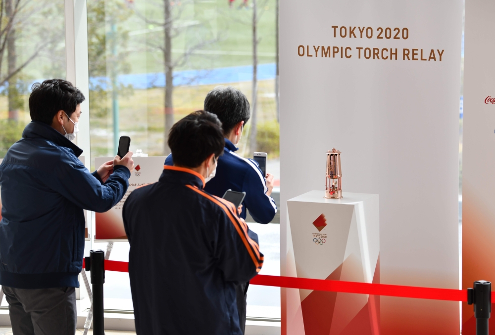 People take pictures in front of the Olympic Flame which was passed from Tokyo 2020 to Fukushima Prefecture at the J-Village National Training Centre in Naraha on April 2, 2020. / AFP / Kazuhiro NOGI