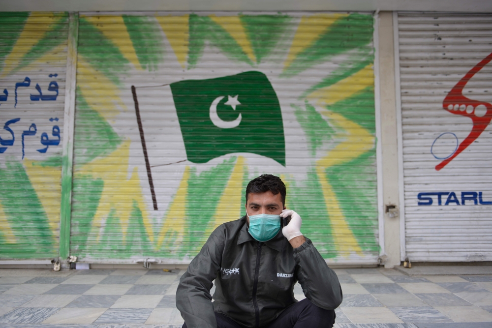 A man wearing a facemask sits in front of a shuttered market during a government-imposed nationwide lockdown as a preventive measure against the COVID-19 coronavirus, in Rawalpindi on April 6, 2020. / AFP / Farooq NAEEM