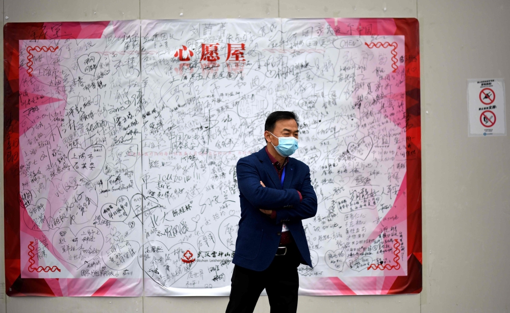 A man wearing a face mask stands in front of a tarpaulin filled with signatures and messages at the Leishenshan Hospital that had offered beds for coronavirus patients in Wuhan, in China’s central Hubei province on April 11, 2020. / AFP / Noel Celis