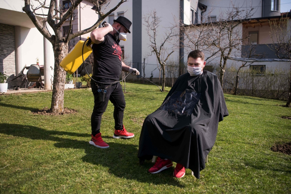 Kosovo hairdresser Driton Kameri (L) wears a facemask as he disinfects a client ahead of a haircut in his garden on March 30, 2020 in Pristina during the time of the COVID-19 pandemic. AFP / Armend NIMANI