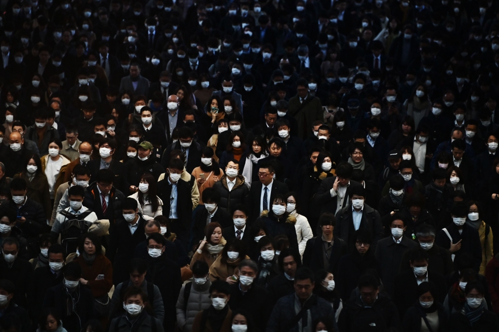 In this file photo taken on February 28, 2020, mask-clad commuters make their way to work during morning rush hour at the Shinagawa train station in Tokyo. Some Japanese office workers are facing a small, but insurmountable hurdle to staying home under th