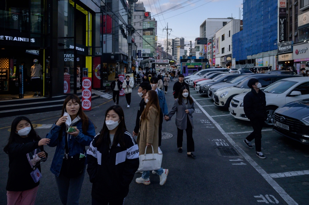 A group of people wearing face masks amid concerns over the COVID-19 novel coronavirus walk along a street in Seoul on April 12, 2020. / AFP / Ed JONES
