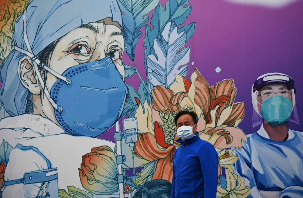 TOPSHOT - A man wearing a face mask walks in front of a mural at the Leishenshan Hospital that had offered beds for coronavirus patients in Wuhan, in China’s central Hubei province on April 11, 2020. / AFP / Noel Celis