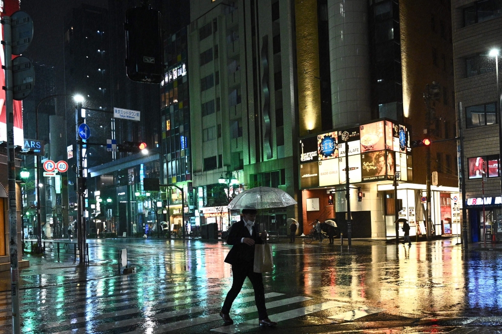 A man wearing a face mask walks with his umbrella in Roppongi district of Tokyo on April 9, 2020. / AFP / Philip FONG