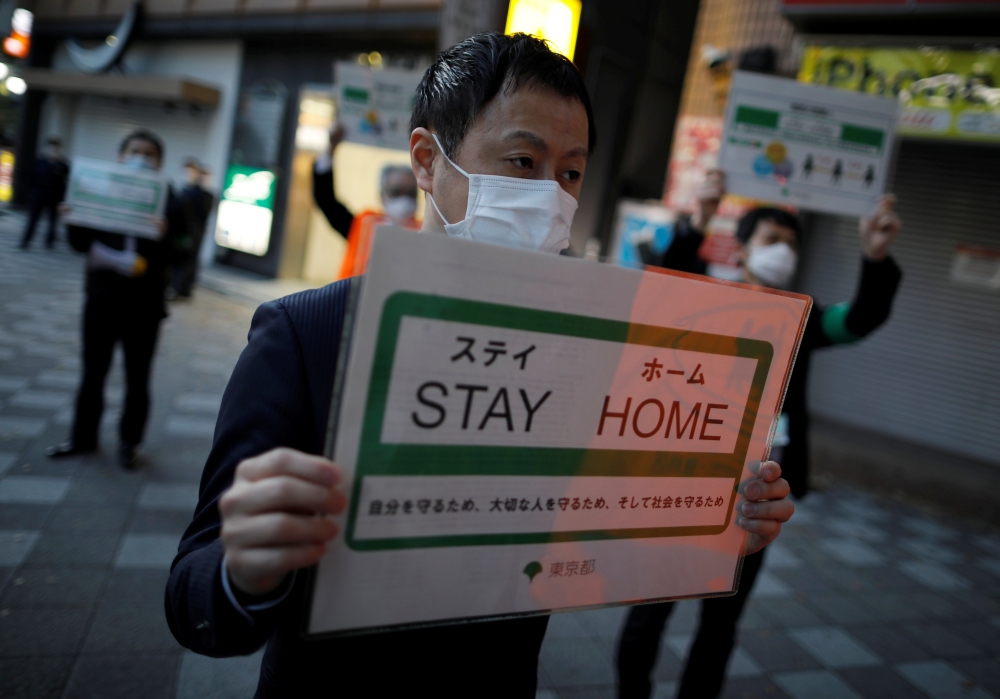 Staff members of the Tokyo metropolitan government wearing face masks hold signs as they call for people to stay home after the government announced the state of emergency for the capital and some prefectures following the coronavirus disease (COVID-19) o