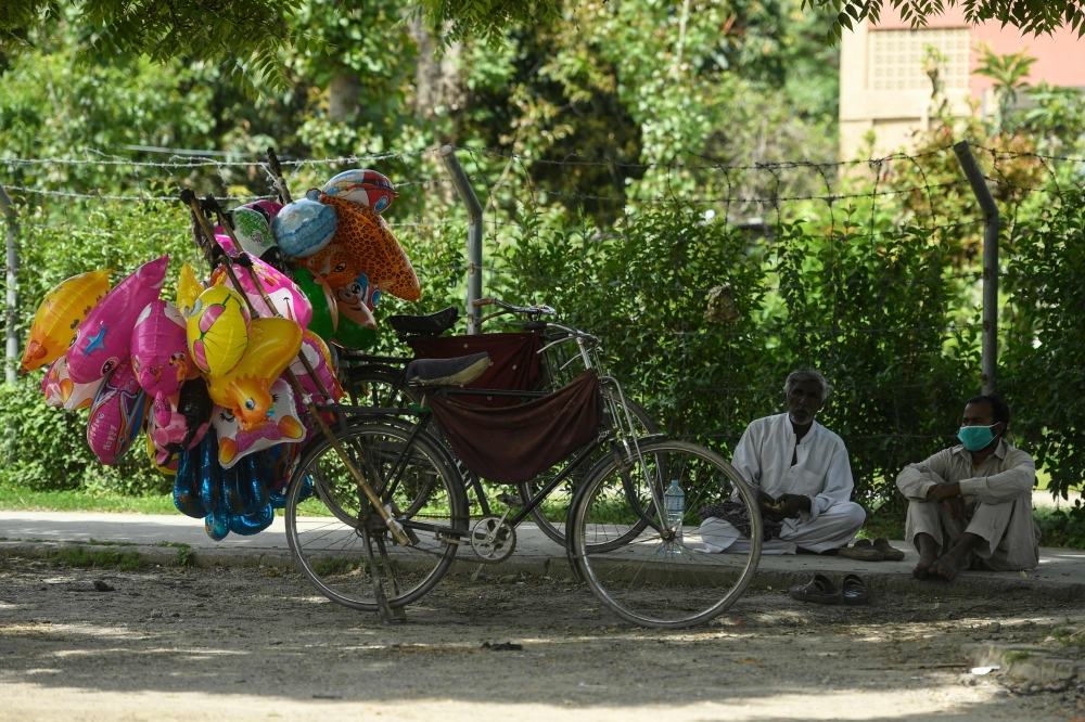 A balloon vendor (R) wearing a facemask waits for customers alongside a street during a government-imposed nationwide lockdown as a preventive measure against the spread of the COVID-19 coronavirus, in Islamabad on April 9, 2020./ AFP / Aamir QURESHI