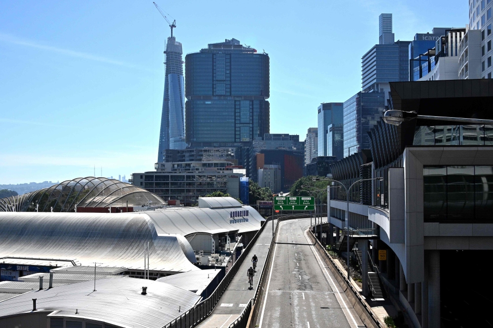 Cyclists (C) make their way through streets made empty by the lockdown restrictions in place due to the COVID-19 coronavirus outbreak in central Sydney on April 15, 2020. / AFP / Saeed KHAN