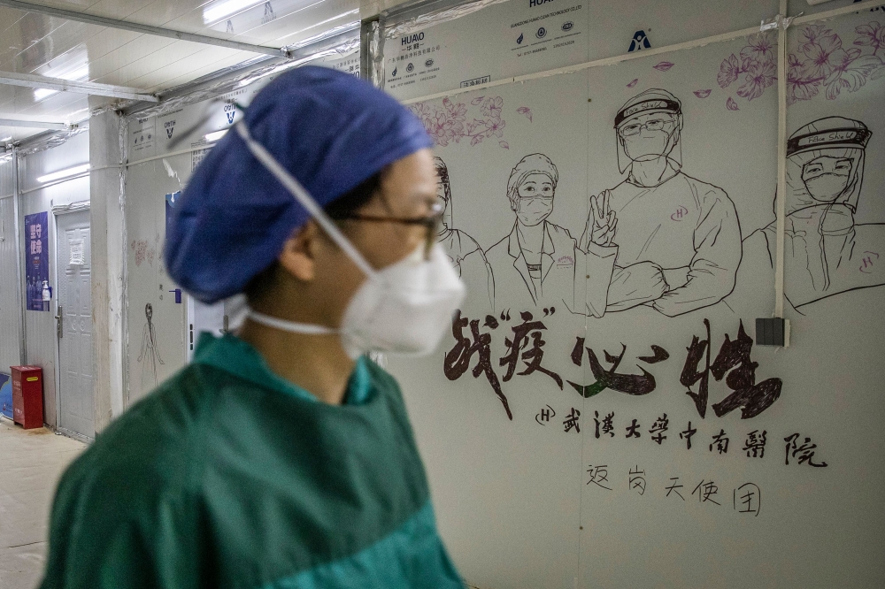 :This photo taken on April 14, 2020 shows a staff member walking past graffiti encouraging people to defeat the COVID-19 coronavirus after all patients left Leishenshan Hospital in Wuhan in China's central Hubei province.  / AFP / STR