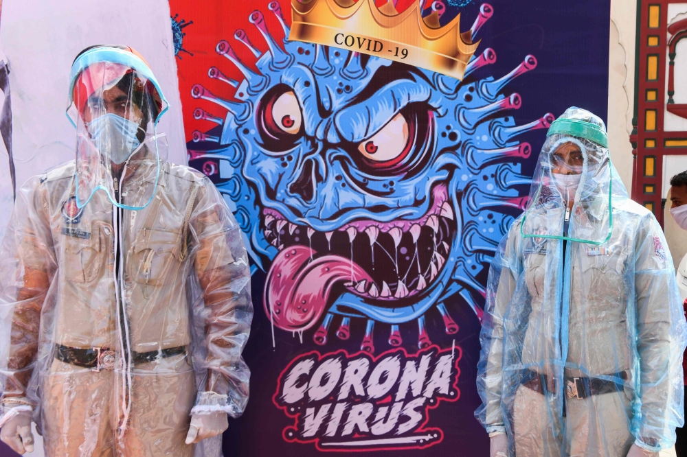 Policemen pose for photos wearing Personal Protective Equipment (PPE)standing next to a poster depicting the COVID-19 coronavirus during an event in Amritsar on April 16, 2020. / AFP / Narinder NANU
