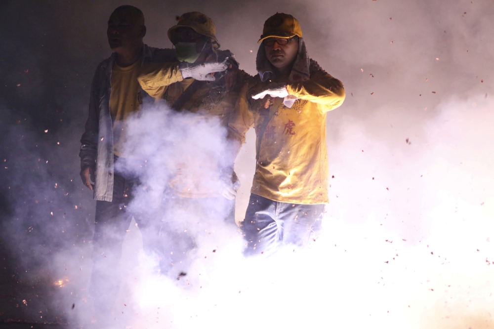 :Devotees, one of them wearing a face mask, walk through the fire crackers to celebrate Mazu's birthday in front of Chaotian Temple in Beigang, amid the spread of the coronavirus disease (COVID-19) in Yunlin, Taiwan on April 15, 2020. REUTERS/Ann Wang