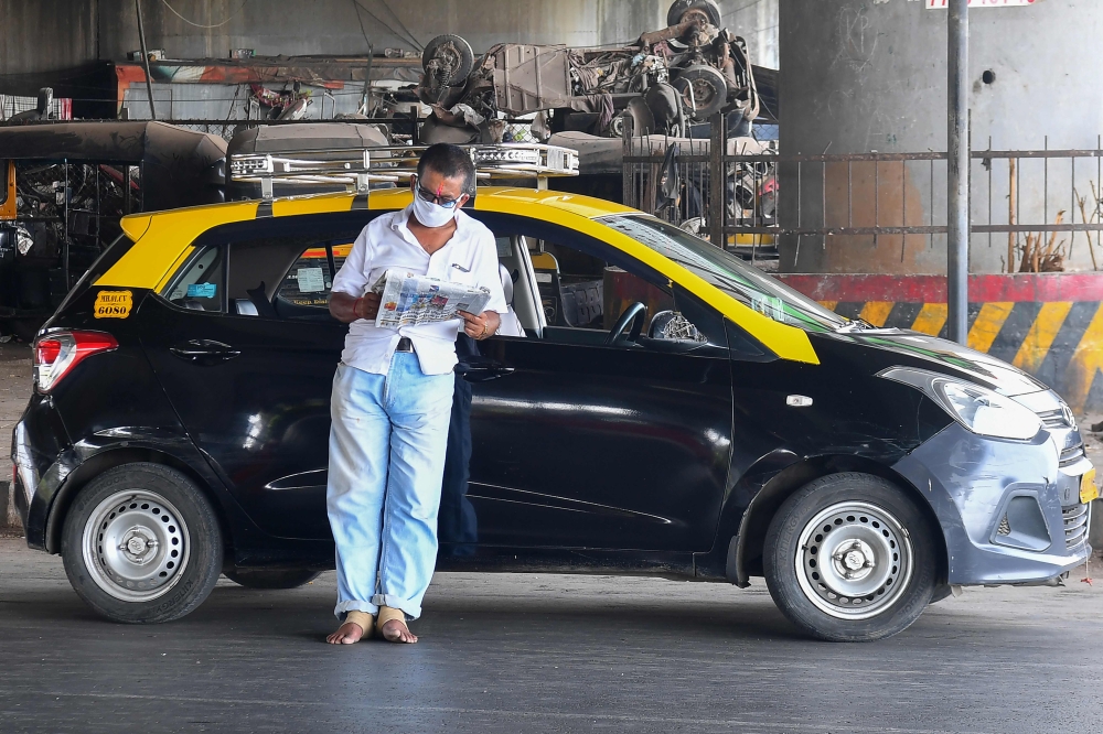 A taxi driver reads a newspaper while waiting for customers under a bridge during a government-imposed nationwide lockdown as a preventive measure against the spread of the COVID-19 coronavirus in MUMBAI on April 17, 2020. / AFP / INDRANIL MUKHERJEE