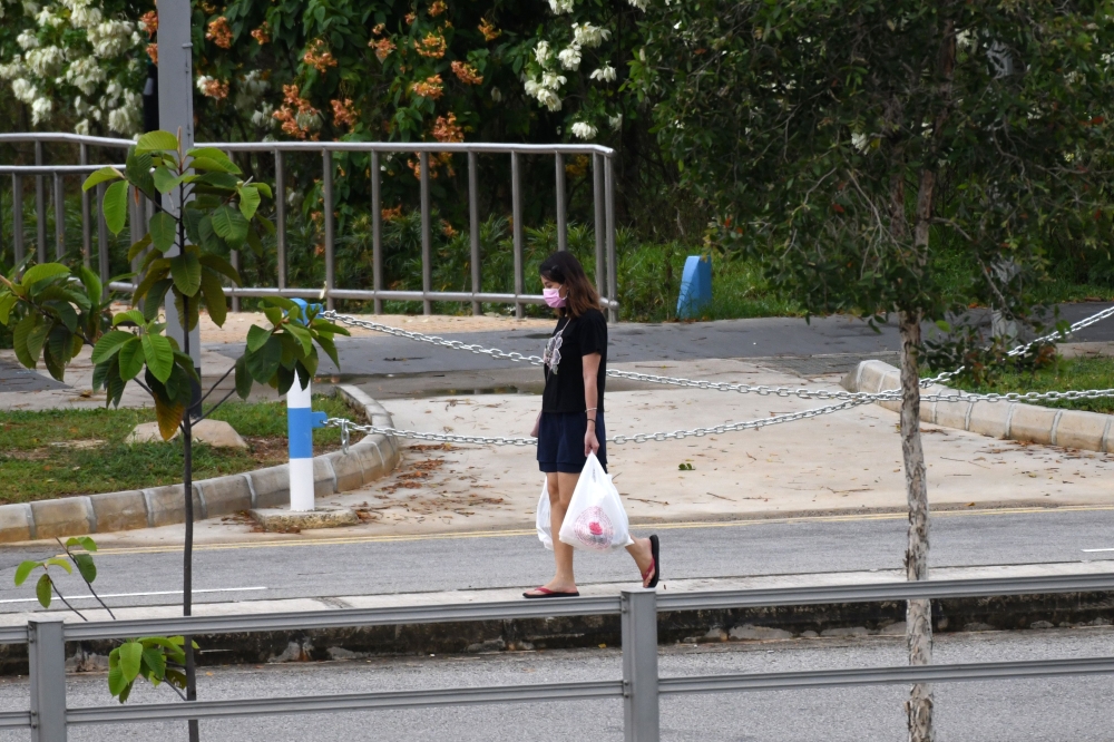 A woman, wearing a face mask as a preventive measure against the spread of the COVID-19 novel coronavirus, carries groceries on her way home in Singapore on April 21, 2020. (AFP / Roslan RAHMAN)