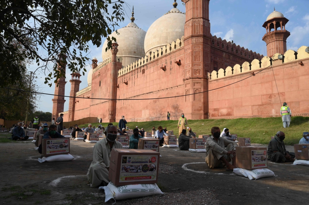 People in need sit maintaining social distancing after collecting free food items outside the Badshahi mosque during a government-imposed nationwide lockdown as a preventive measure against the COVID-19 coronavirus, in Lahore on April 21, 2020. / AFP / AR