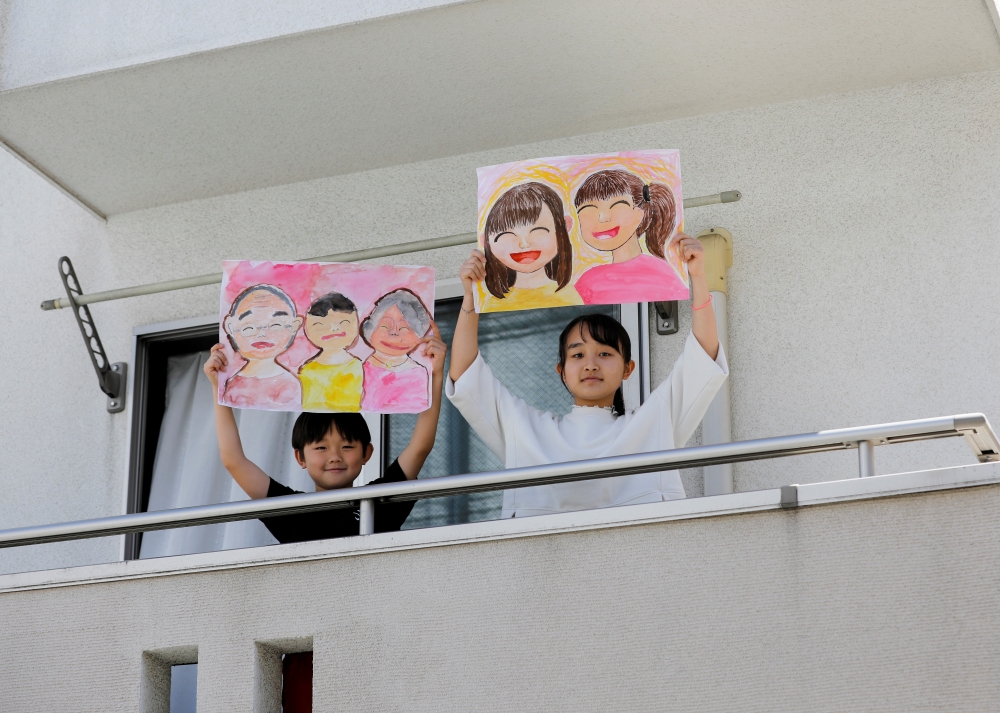 Reku Matsui, 8, and Yaya Matsui, 12, pose for a photograph while holding pictures that they drew during the coronavirus disease (COVID-19) outbreak, as they stand on the balcony of their home in Tokyo, Japan, April 19, 2020. REUTERS/Kim Kyung-Hoon 