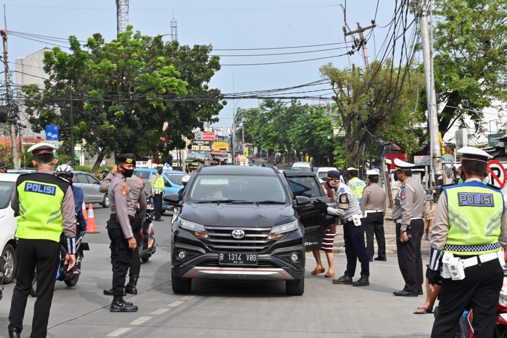 :Indonesian policemen check passengers in their vehicle at the border between Jakarta and Tangerang after the government imposed a large-scale social restrictions to curb the spread of the COVID-19 coronavirus in Jakarta on April 27, 2020. / AFP / ADEK BE