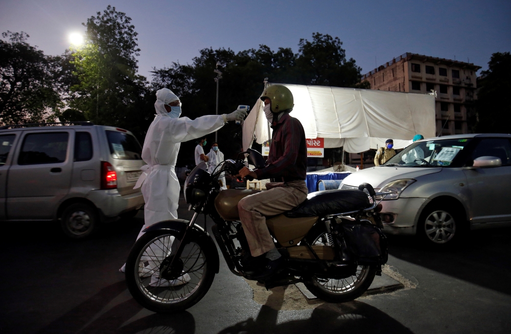 A health worker uses an infrared thermometer to measure the temperature of a motorcyclist on a road during a nationwide lockdown to slow the spreading of the coronavirus disease (COVID-19) in Ahmedabad, India, April 27, 2020. REUTERS/Amit Dave