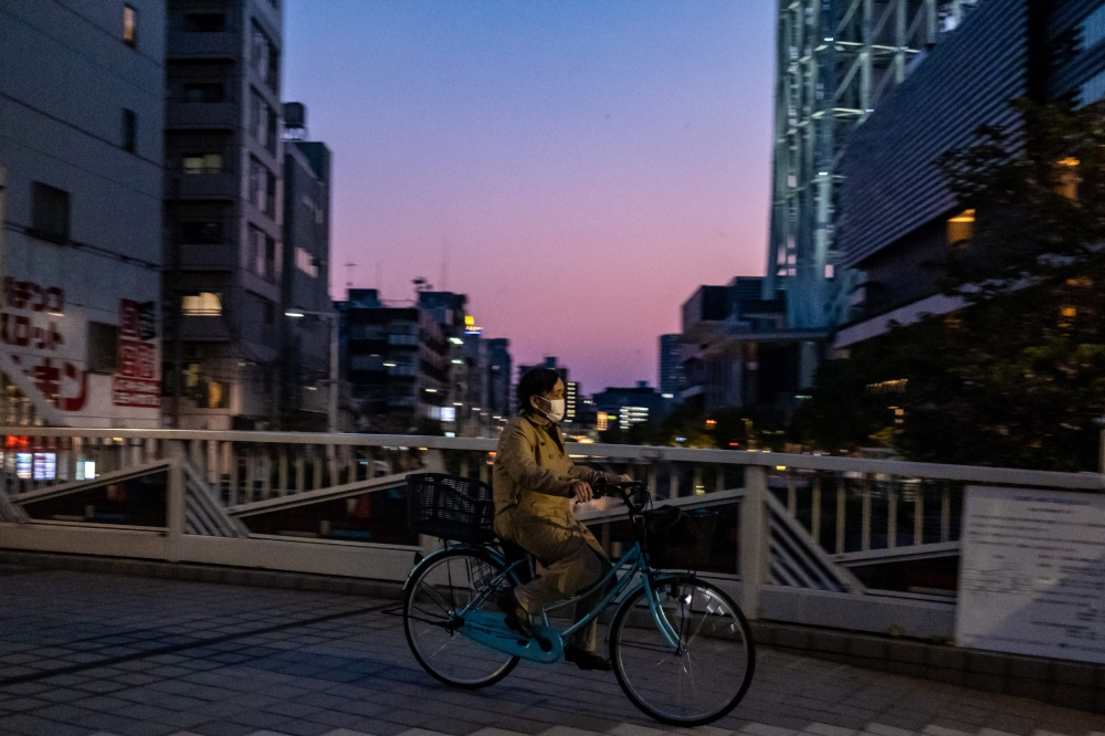 A woman wearing a face mask rides a bicycle in Tokyo on April 29, 2020. / AFP / Philip FONG