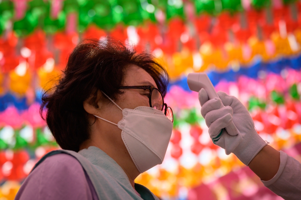 Worshippers wearing face masks have their temperature taken as they attend a prayer ceremony entitled 'overcoming and healing the COVID-19 coronavirus', while marking Buhha's birthday at the Jogye buddhist temple in Seoul on April 30, 2020. / AFP / Ed JON