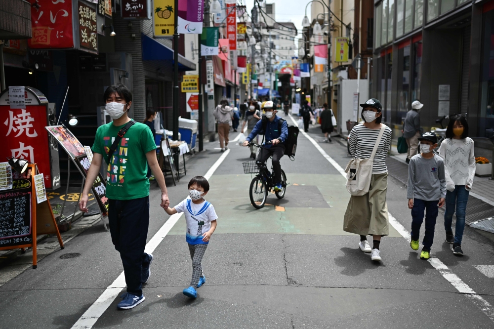 TOPSHOT - People walk past shops in a residential area in Tokyo on May 4, 2020. / AFP / CHARLY TRIBALLEAU

