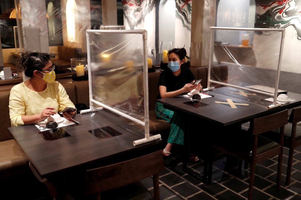 Women are seen at a Taiwanese hot pot style restaurant that reopened after the easing of restrictions with the implementation of a plastic barrier and social distancing measures to prevent the spread of the coronavirus disease (COVID-19) in Bangkok, Thail