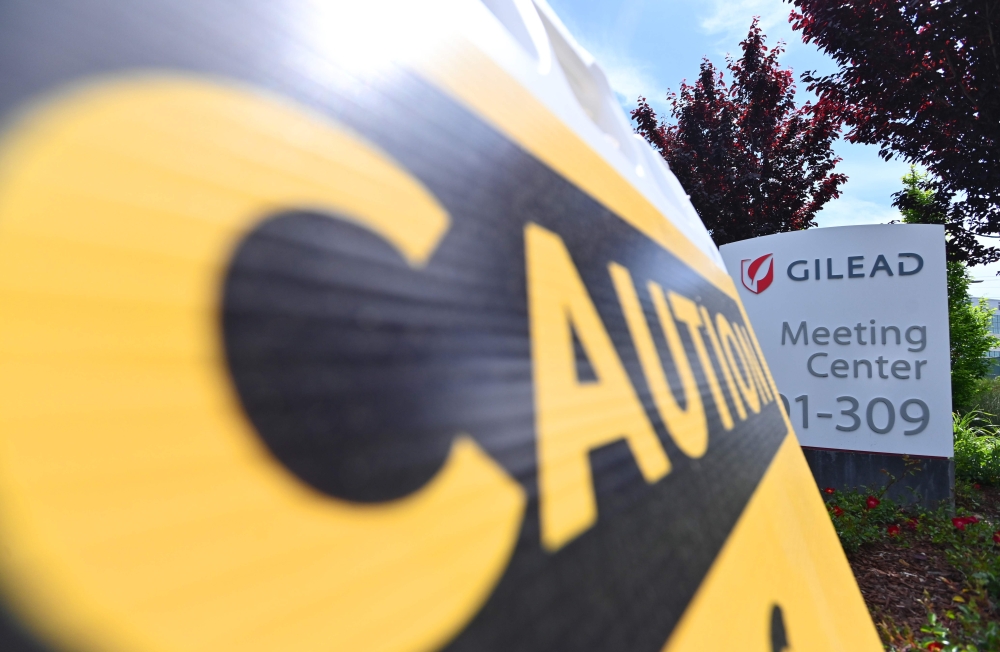 A caution sign sits on a sidewalk in front of the Gilead Sciences headquarters in Foster City, California on April 30, 2020. Gilead Science's remdesivir, one of the most highly anticipated drugs being tested against the new coronavirus, showed positive re