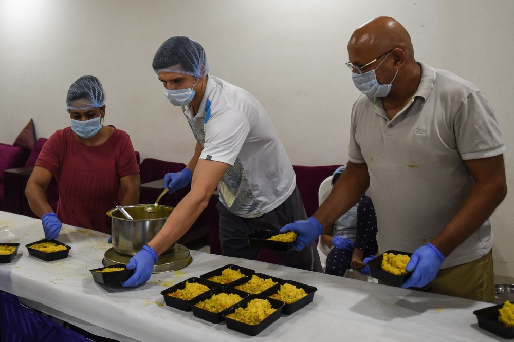 Moldovan tennis player Dmitrii Baskov (C) packs food to be distributed to people in need along with Director of Ace Tennis Academy Pramesh Modi (R) and Founder of Shree Sava Foundation Ami Pramesh Modi during nationwide lockdown as a preventive measure ag
