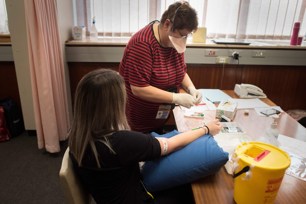 :Michelle van Rooyen (R), a staff member gets ready to take a blood sample from a volunteer at the start of a clinical trial being set up by TASK, a clinical research organisation based in Cape Town, to see whether the Bacillus Calmette-Guerin (BCG) vacci