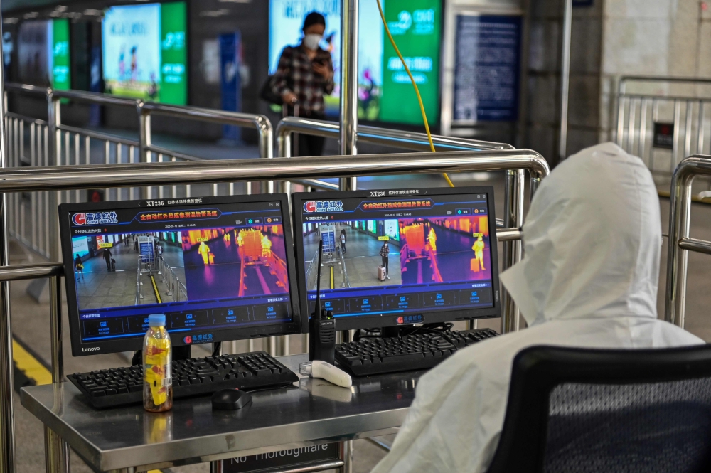 A worker wearing protective gear watches screens showing the body temperature of arriving passengers at Hankou railway station in Wuhan, Hubei Province on May 12, 2020. / AFP / Hector RETAMAL
