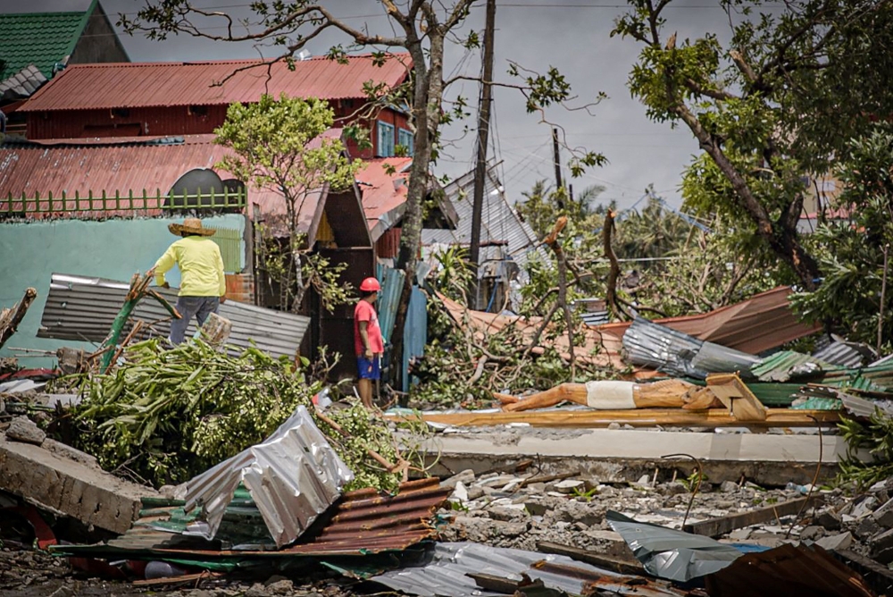 Residents stand amongst debris and next to a huge crucifix blown from the church after it was destroyed at the height of typhoon Vongfong in Arteche town, Eastern Samar province on May 15, 2020, a day after the typhoon hit the town. typhoon Vongfong has d
