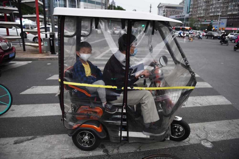 A man and a boy wear face masks as a precaution against the COVID-19 coronavirus as they wait to cross a road in Beijing on May 15, 2020. / AFP / GREG BAKER
