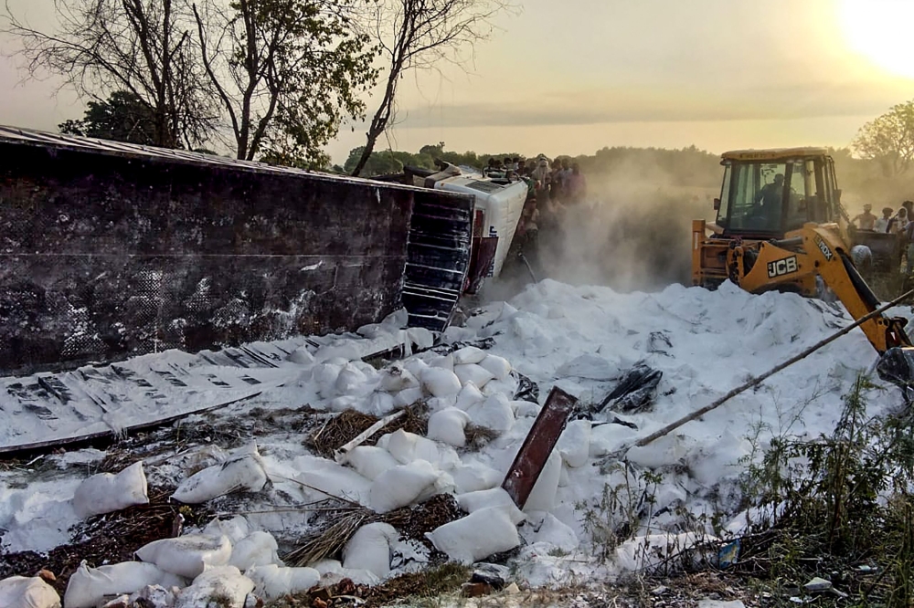 Rescue workers and people stand watching as an excavator gathers the wreckage of a truck transporting goods and migrant labourers going back to their hometowns after it collided with another vehicle, in Auraiya district of Uttar Pradesh state on May 16, 2