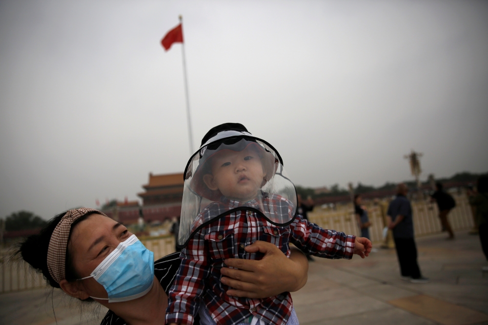 :A woman holds a child who wears a protective face cover as they pose for pictures near a Chinese national flag at the Tiananmen Square in Beijing, following the novel coronavirus disease (COVID-19) outbreak, China May 16, 2020. REUTERS/Tingshu Wang
