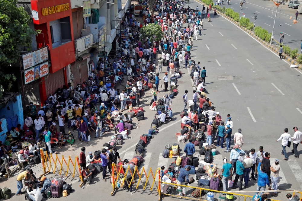 Migrant workers and their families wait for transport to reach to a railway station to board a train to their home state of northern Uttar Pradesh, after a limited reopening of India's giant rail network following a nearly seven-week lockdown to slow the 