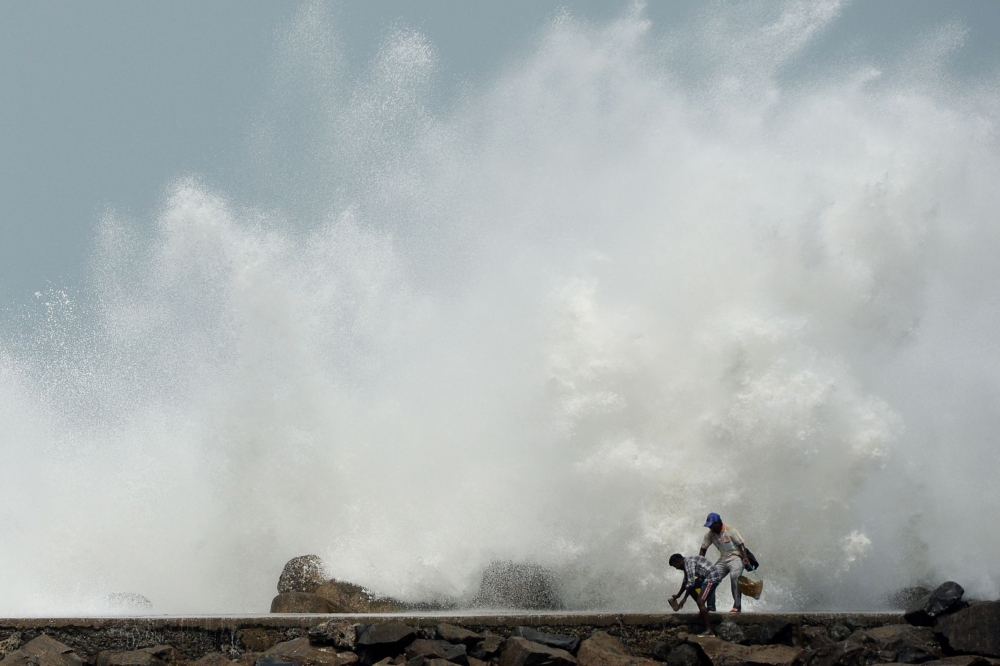 Men walk past as waves hit a breakwater at Kasimedu fishing harbour in Chennai on May 19, 2020, as Cyclone Amphan barrels towards India's eastern coast. / AFP / Arun SANKAR
