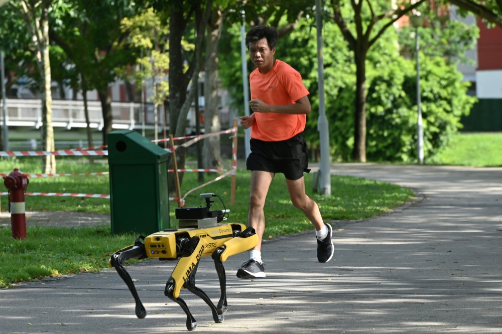 (FILES) In this file photo taken on May 8, 2020, a man jogs past a four-legged robot called Spot, which broadcasts a recorded message reminding people to observe safe distancing as a preventive measure against the spread of the COVID-19 coronavirus, durin