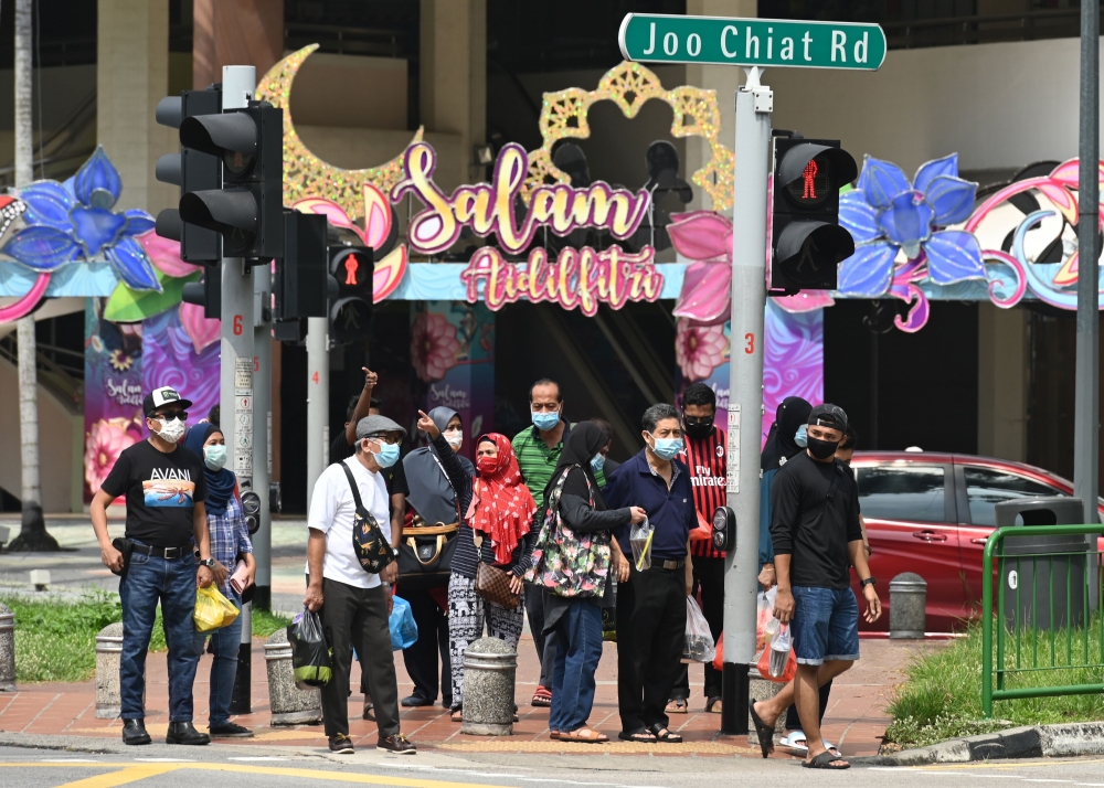 People wearing face masks amid concern over the spread of the COVID-19 coronavirus wait at a road crossing with building displays of festive decorations ahead of Eid al-Fitr which marks the end of the Muslim holy month of Ramadan, at the Geylang Serai mar