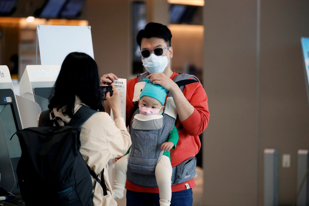 FILE PHOTO: A woman wearing a mask to avoid the spread of the coronavirus disease (COVID-19) takes a photograph of her husband and child after checking in at Gimpo international airport in Seoul, South Korea, May 1, 2020. REUTERS/Kim Hong-Ji/File Photo
